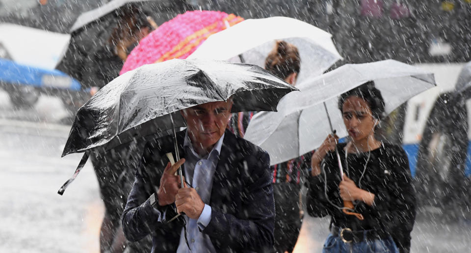 heavy rain pouring down on people trying to stay dry with umbrellas 