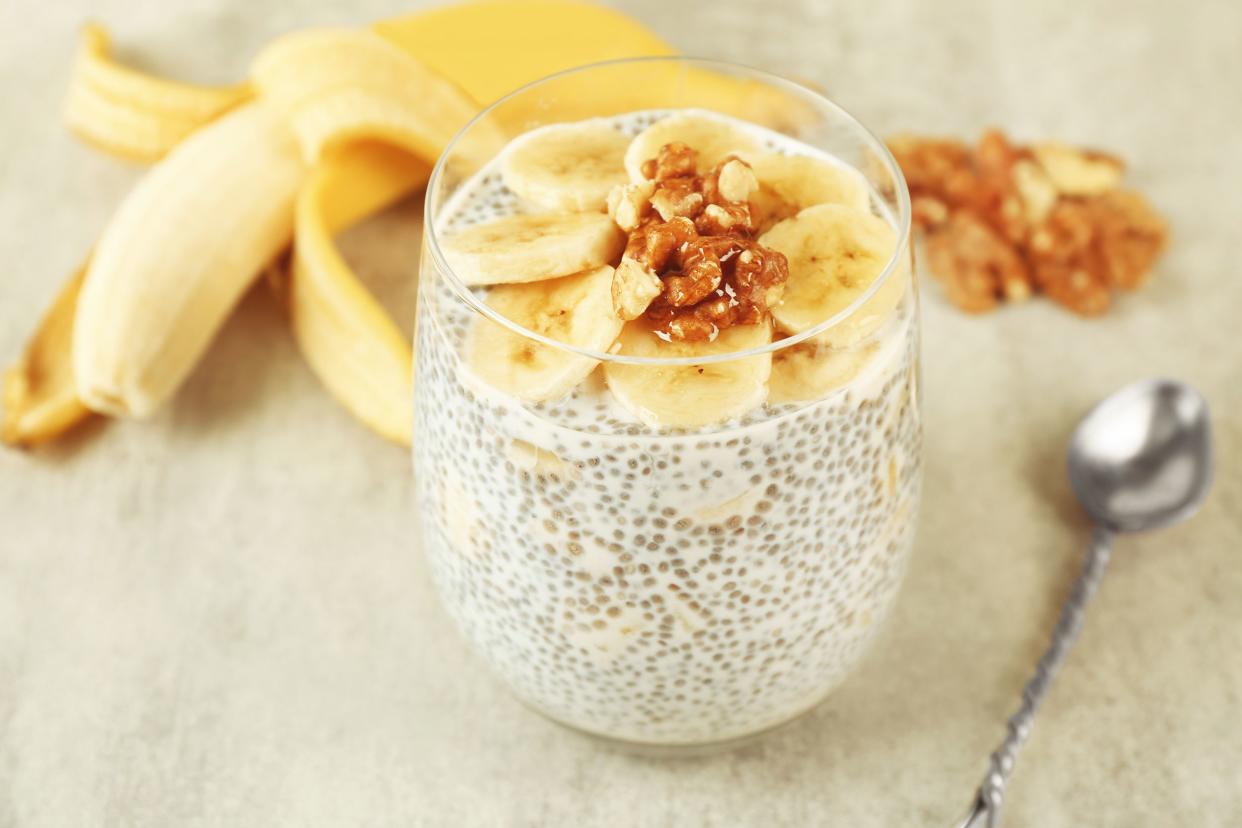 Banana chia pudding in a glass serving cup with a blurred background of a banana, pecans, and a spoon