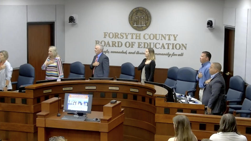 In this image from video posted by the Forsyth County school board, attendees recite the Pledge of Allegiance during a board meeting in Cumming, Ga., on June 20, 2023. A Georgia law passed by Republican lawmakers has made it easier for parents to challenge school library books as inappropriate. The Forsyth County school board has ruled parents must give advance permission before any student can read five of the challenged books. (Forsyth County Schools via AP)
