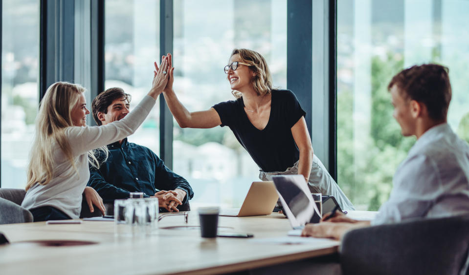 ADHD Female professional giving a high five to her colleague in conference room. Group of colleagues celebrating success in a meeting.