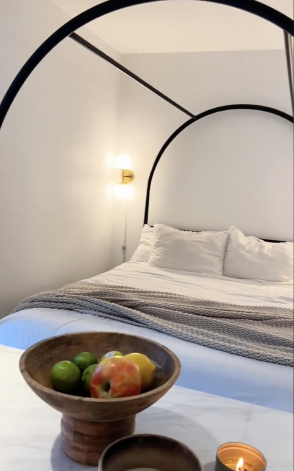 A minimalist bedroom with a circular frame headboard, striped blanket, bowl of fruit on the side table, and a lit candle