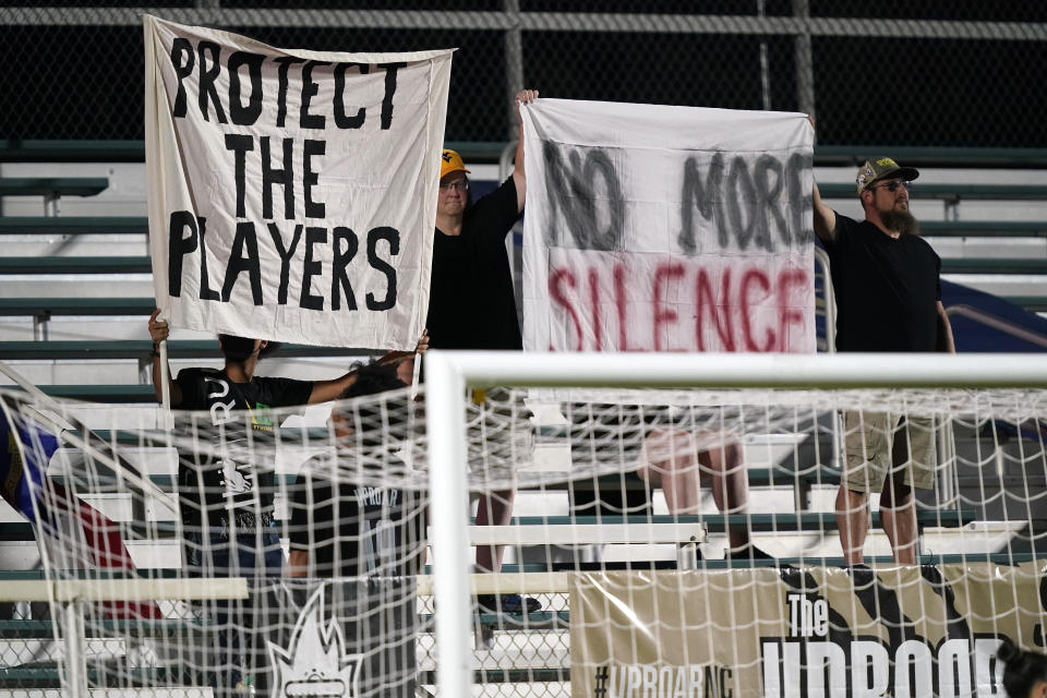 Fans hold signs during the first half of an NWSL soccer match between the North Carolina Courage and Racing Louisville FC in Cary, N.C., Wednesday, Oct. 6, 2021. (AP Photo/Gerry Broome)