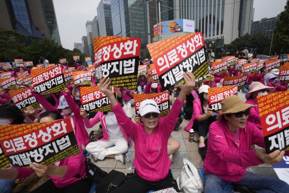 People in deep pink clothing hold up signs in Korean
