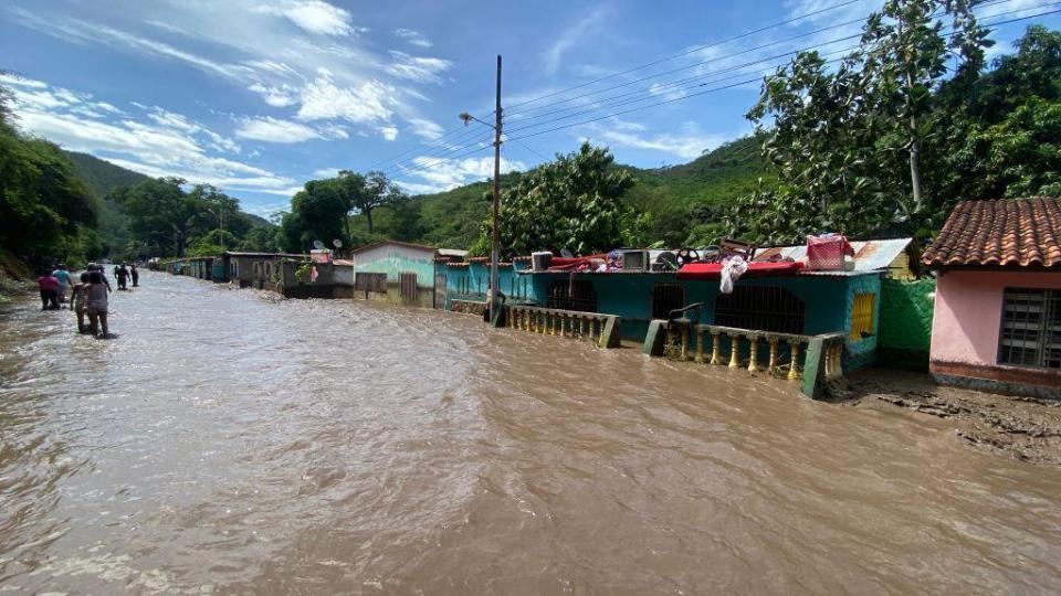  People stand outside their flooded homes after a river swelled due to heavy rains following the passage of Hurricane Beryl on the road from Cumana to Cumanacoa, Sucre State, Venezuela, on July 2, 2024