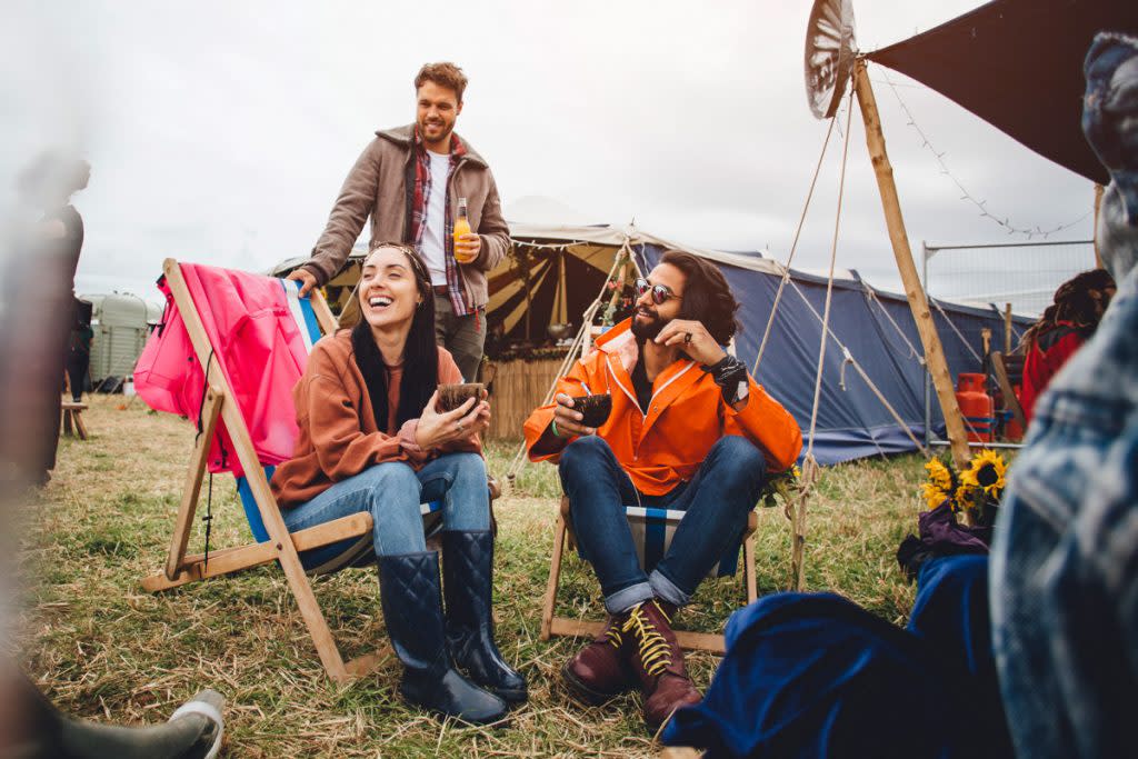 People sip on drinks while sitting in lawn chairs at a camp site at a music festival. 