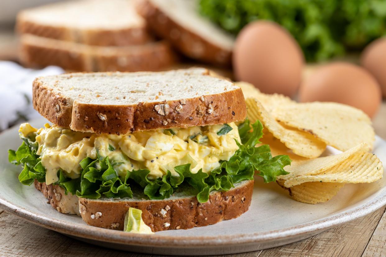 Closeup of egg salad and lettuce sandwich on whole grain bread with potato chips on a plate