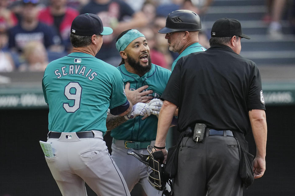 Seattle Mariners' J.P. Crawford, second from left, is held back by manager Scott Servais (9) and third base coach Manny Acta, second from right, after being ejected by home plate umpire Doug Eddings, right, during the fifth inning of a baseball game Wednesday, June 19, 2024, in Cleveland. (AP Photo/Sue Ogrocki)