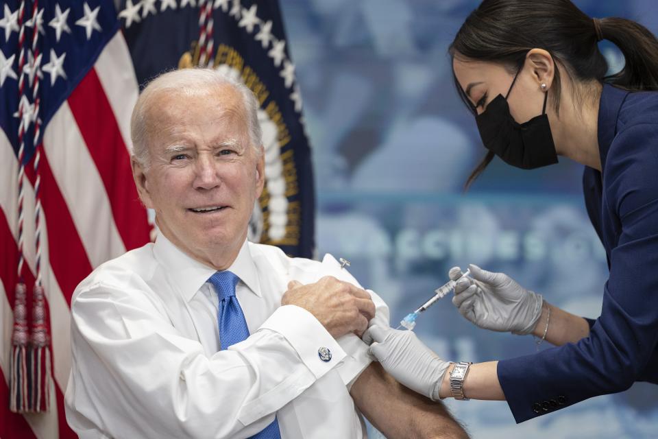 In front of a U.S. flag, President Biden pulls up his sleeve as he receives a COVID-19 booster shot at the White House on Oct. 25. 