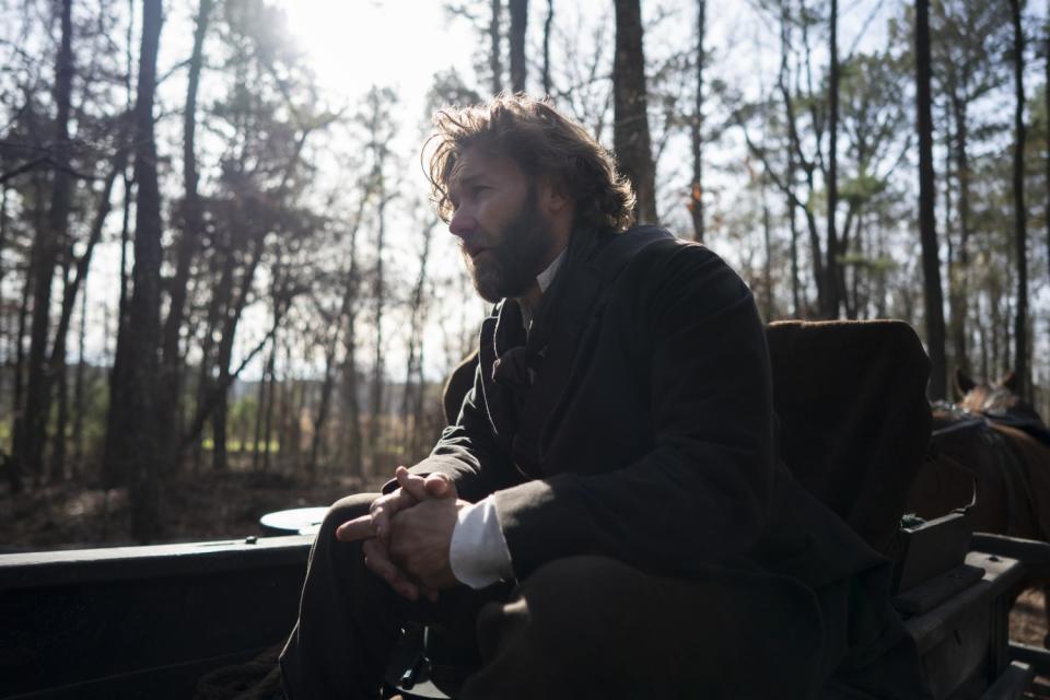 A bearded man in a horse-drawn carriage in the woods