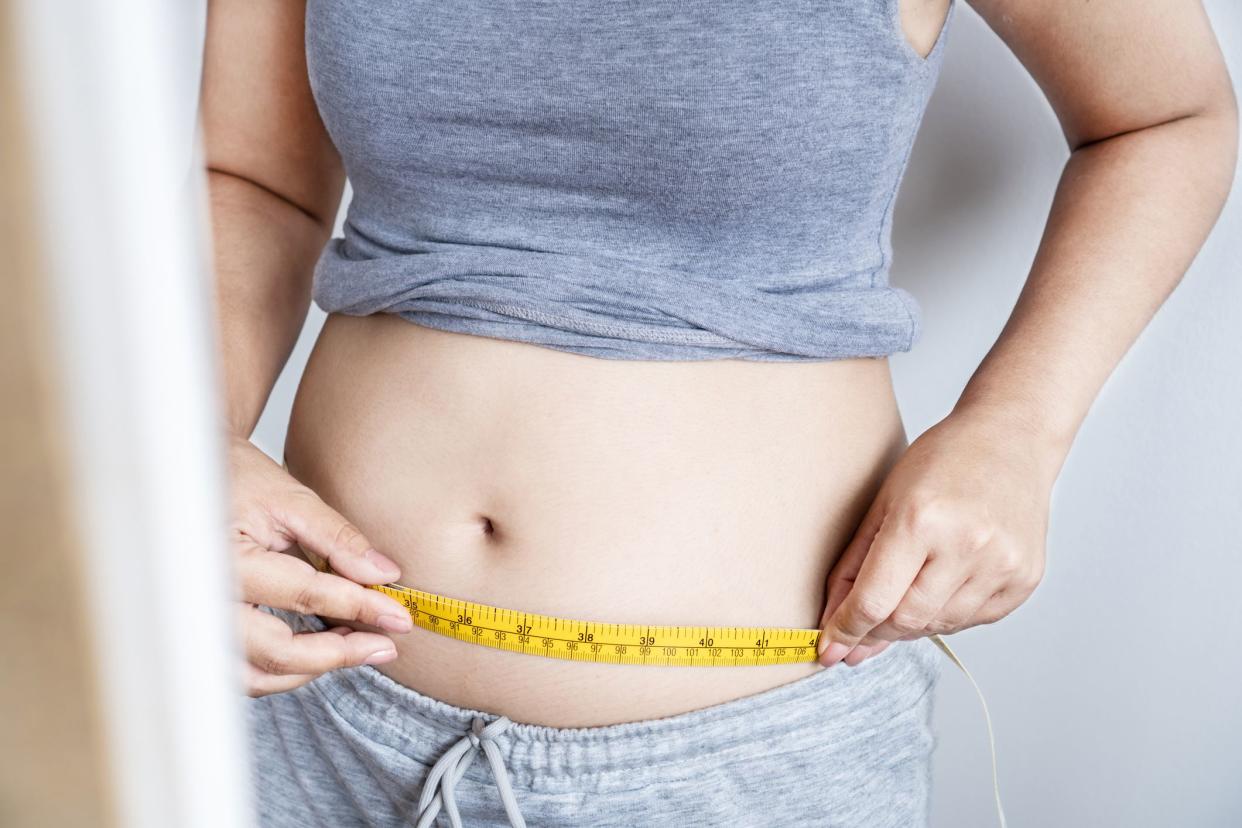 closeup obese woman checking her fat  belly with a measuring tape in front of a mirror