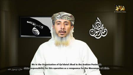 Nasser bin Ali al-Ansi, a leader of the Yemeni branch of al Qaeda (AQAP), speaks as an image of the Islamic State flag (rear L) is seen in this still image taken from a social media website on January 14, 2015, which purports to show Al Qaeda in Yemen claiming responsibility for the attack on French satirical newspaper Charlie Hebdo. REUTERS/YouTube via Reuters