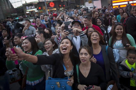 People react as their image is projected on a billboard owned by Revlon that takes their pictures and displays them in Times Square in the Manhattan borough of New York October 13, 2015. REUTERS/Carlo Allegri