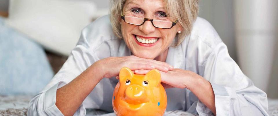 Conceptual portrait of happy senior female lying on bed with piggybank