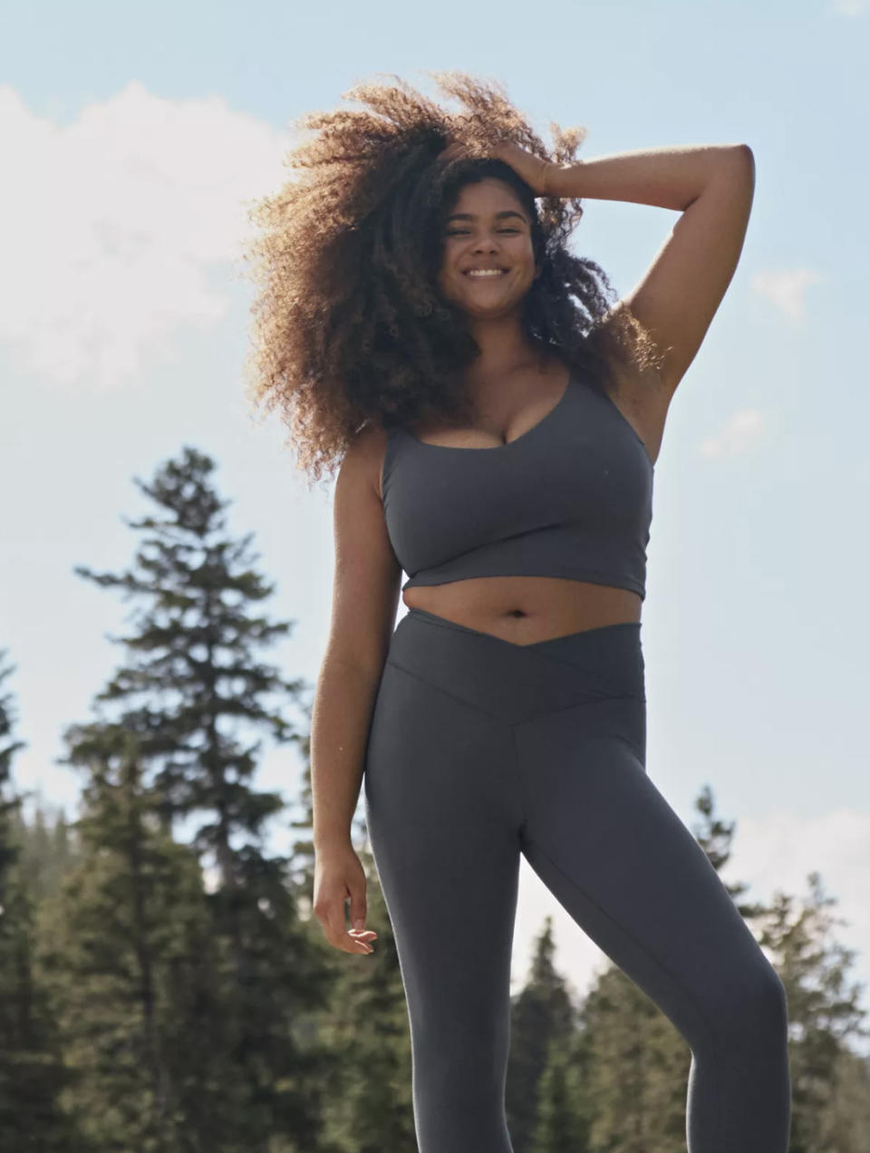 Model posing outside with hip popped wearing grey sports bra with matching crossover leggings