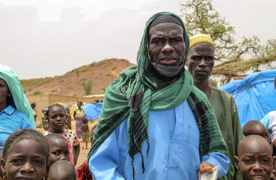 Volunteer fighter Issa Tamboure, walks with his family outside his tent in a makeshift site for displaced people in Kongoussi, Burkina Faso, Thursday, June 4, 2020. With little training, few weapons, and dwindling means amid an economic downturn fueled by the coronavirus pandemic, volunteers like Tamboure, recruited by the military to help fight jihadists, say they struggle to battle the well-armed extremists. (AP Photo/Sam Mednick)