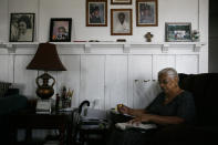 Lavarn Young, 81, reads her bible in the living room of her home as framed photos of herself, far left, and relatives adorn a wall Tuesday, July 14, 2020, in the Watts neighborhood of Los Angeles. Young, who moved to Watts from Texas in 1946, said she's seen a lot of good change since the 1965 rebellion. But she said gangs had made the neighborhood more dangerous than it was a half century ago. (AP Photo/Jae C. Hong)