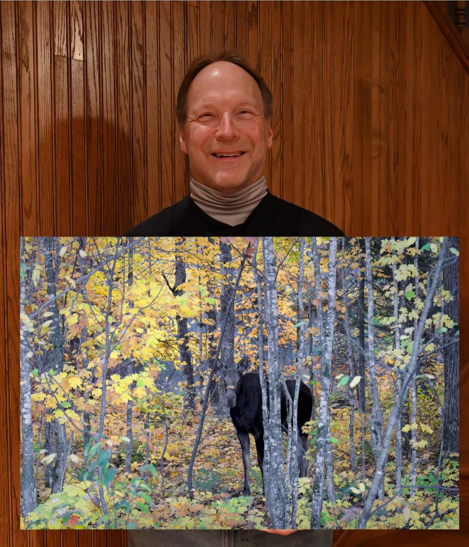 Charlie Rumschlag, also an Artist of the Month for the Monroe Art League, holds one of his photographs. This photo, showing moose, was taken in the western part of the Upper Peninsula.