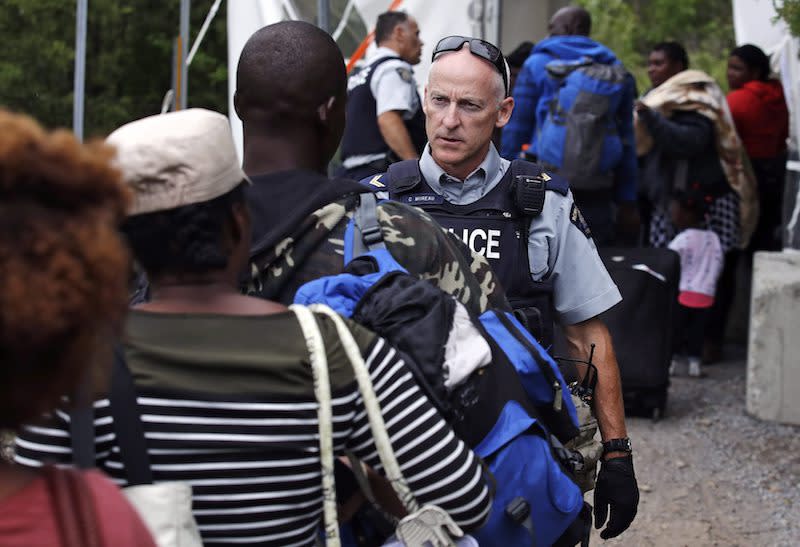 A Royal Canadian Mounted Police officer standing in Saint-Bernard-de-Lacolle, Que., advises migrants that they are about to illegally cross from Champlain, N.Y., and will be arrested on Aug. 7, 2017. Photo from Charles Krupa/The Associated Press.