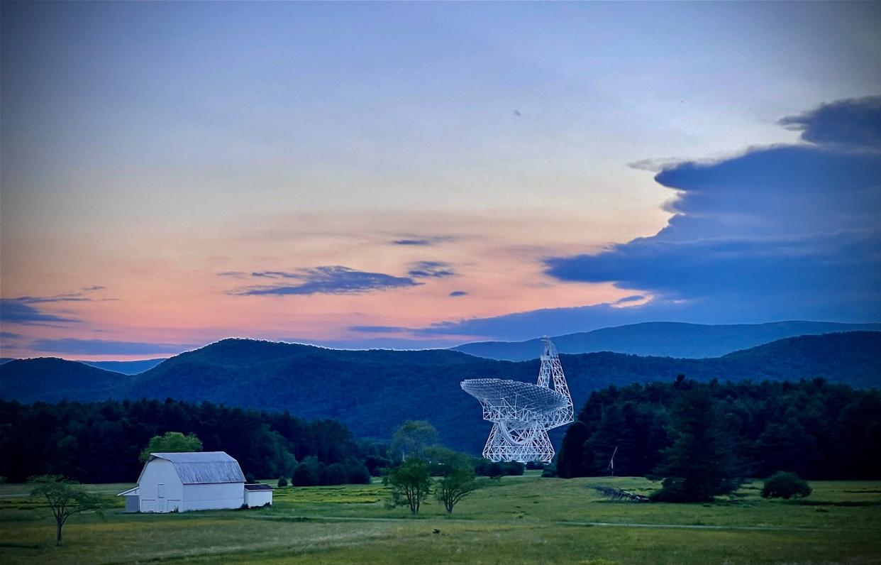 a large telescope sits in a green field next to a white barn in a rural setting