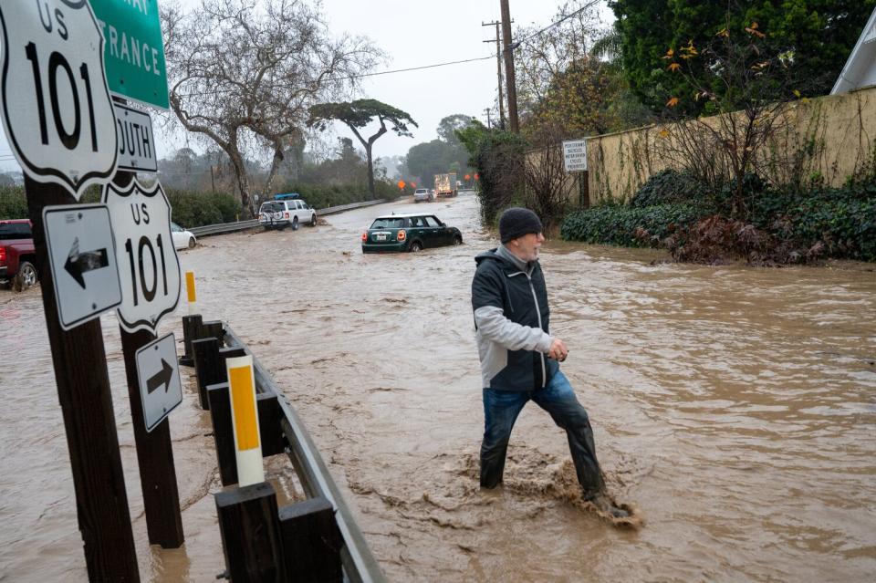 A man walks on a flooded road, with water covering his feet.