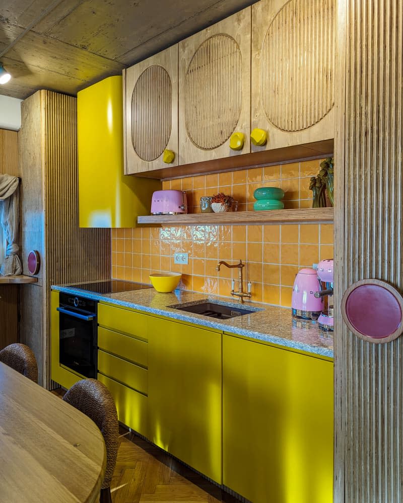 Yellow kitchen with fluted wood cabinets, parquet floor, window bar and dining table