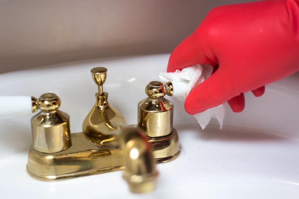 Person wearing red rubber glove polishing a brass bathroom faucet