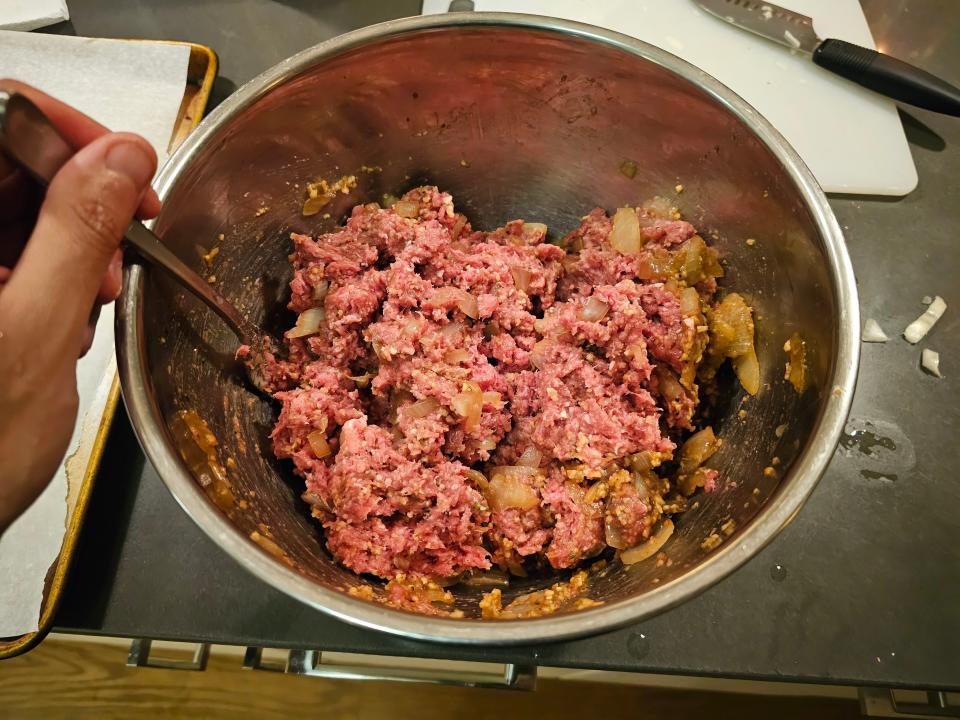 Ground beef mixed with browned onions in a metal bowl