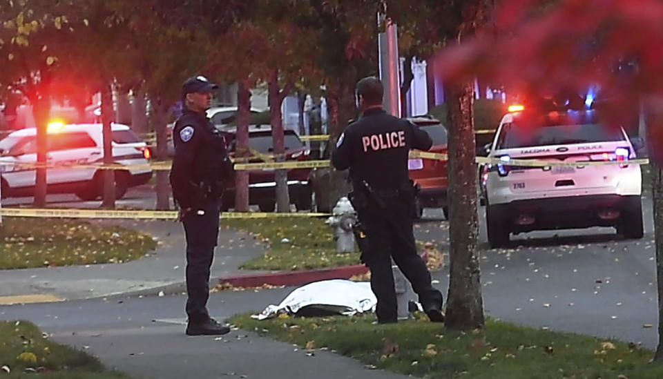 Tacoma police stand by a covered body at the scene of a shooting in Tacoma, Wash. Thursday, Oct. 21, 2021. Four people were killed in a shooting in Tacoma on Thursday afternoon, police said.(Drew Perine/The News Tribune via AP)