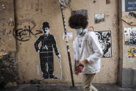 A man wearing a face mask, walks by a Charlie Chaplin street art, in the Montmartre district of Paris, Sunday Oct.25, 2020. A curfew intended to curb the spiraling spread of the coronavirus, has been imposed in many regions of France including Paris and its suburbs. (AP Photo/Lewis Joly)