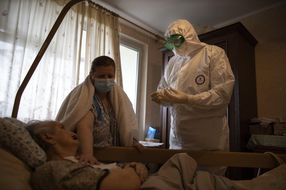 In this photo taken on Monday, June 1, 2020, Father Vasily Gelevan, wearing a biohazard suit and gloves to protect against the coronavirus, prepares to give Holy Communion to Lyudmila Polyak, 86, who is suspected of being infected with coronavirus, at her apartment in Moscow, Russia. In addition to his regular duties as a Russian Orthodox priest, Father Vasily visits people infected with COVID-19 at their homes and hospitals. (AP Photo/Alexander Zemlianichenko)