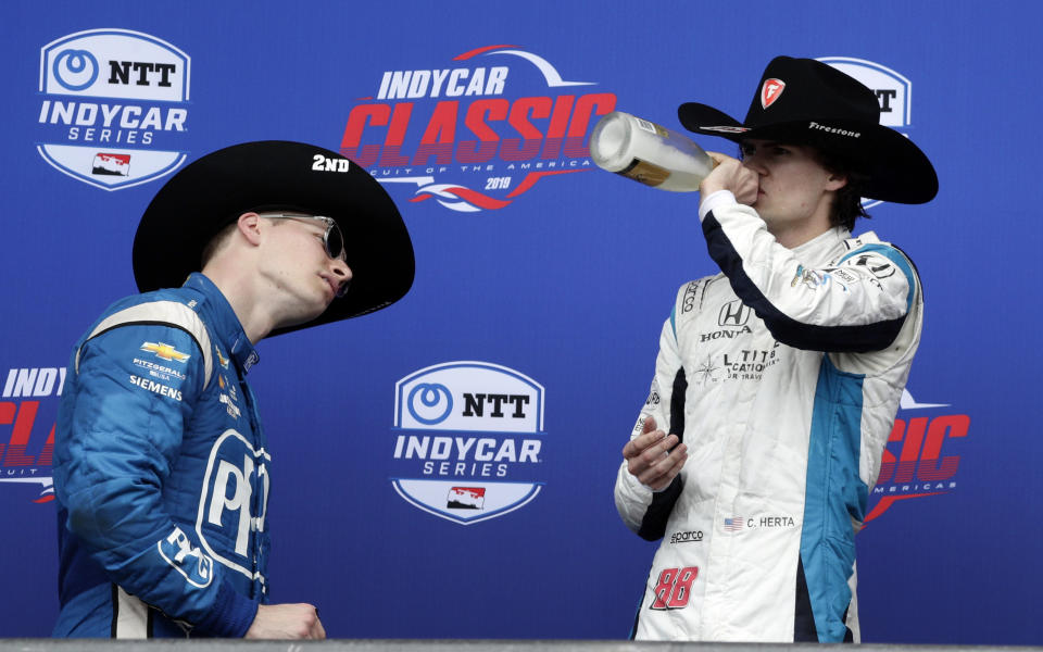 Colton Herta, right, takes a celebratory swig after winning the IndyCar Classic auto race, as second-place finisher Josef Newgarden, left, takes a closer look a the bottle label Sunday, March 24, 2019, in Austin, Texas. Herta, 18, became the youngest winner in IndyCar history after a late-race crash near the entry to pit row helped him steal past the leaders to the checkered flag. (AP Photo/Eric Gay)