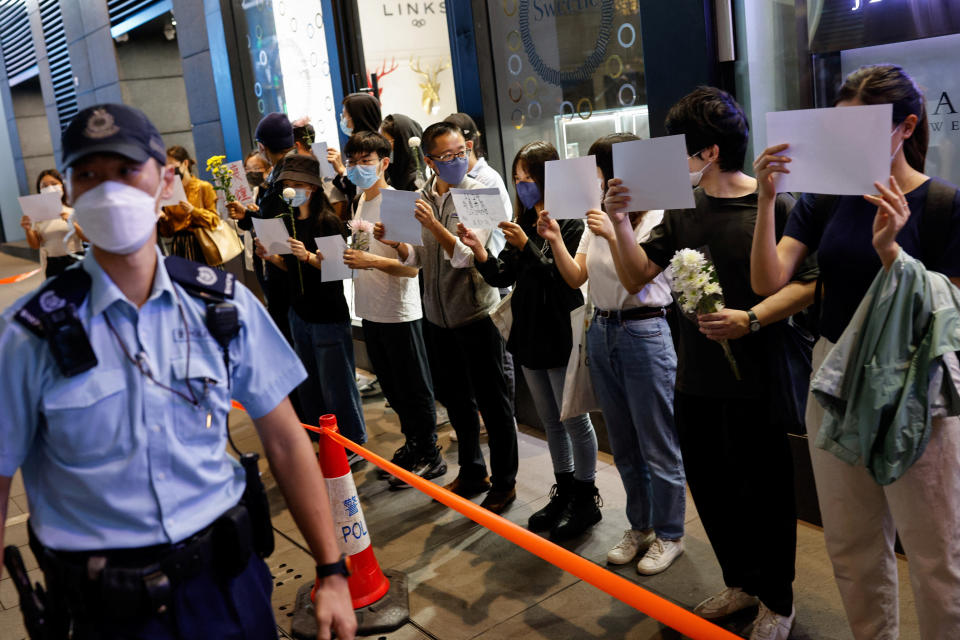 People hold white sheets of paper and flowers in a row as police check their IDs during a protest over coronavirus disease (COVID-19) restrictions in mainland China, during a commemoration of the victims of a fire in Urumqi, in Hong Kong, China November 28, 2022. REUTERS/Tyrone Siu