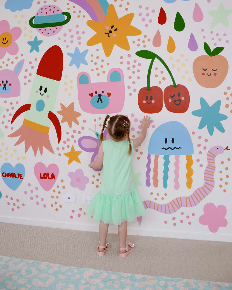 child putting her hand on a wall with a colorful mural design