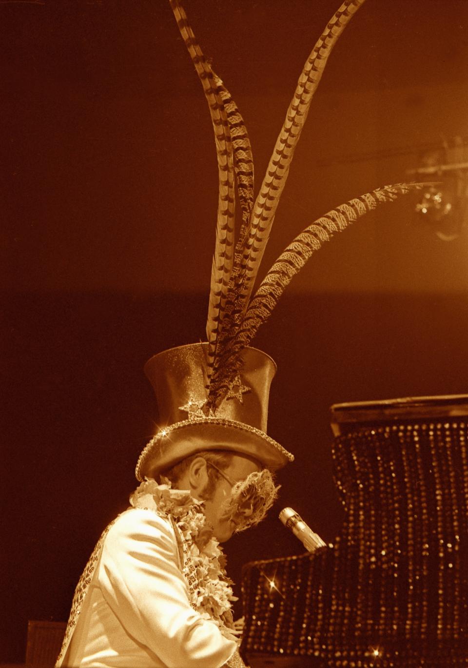 John performs onstage in a feathered hat.&nbsp;