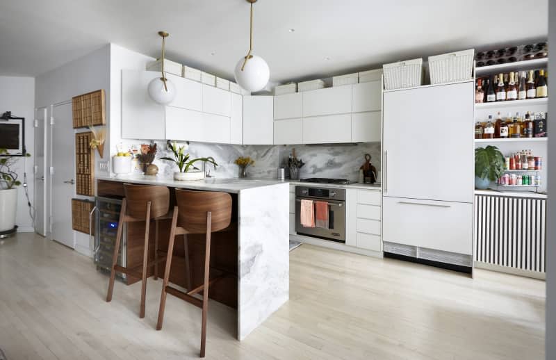 Kitchen with marble bar/counter/backsplash, curve-backed wooden stools, white cabinets, fridge, white globe pendant lights