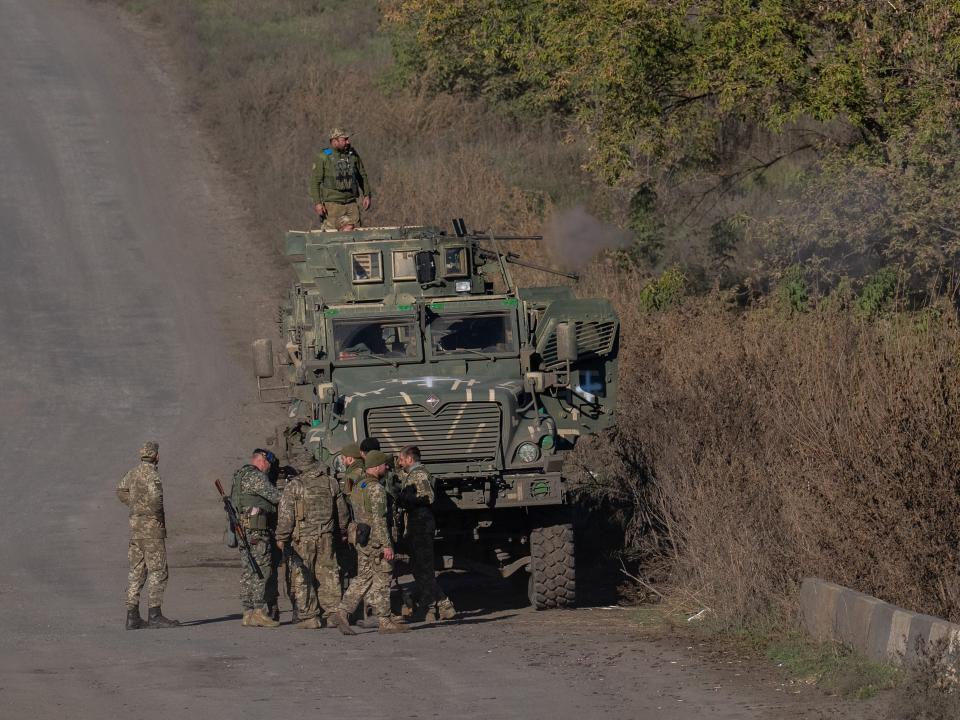 soldiers in camouflage near armored vehicle on dirt road