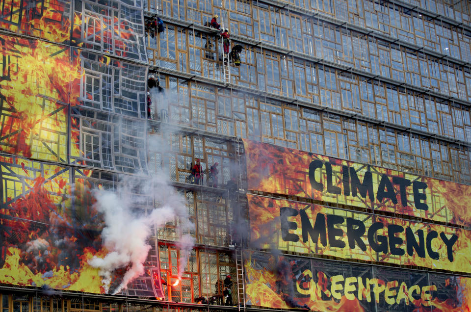 Climate activists send off smoke flares from behind a banner on the Europa building during a climate demonstration outside an EU summit meeting in Brussels, Thursday, Dec. 12, 2019. Greenpeace activists on Thursday scaled the European Union's new headquarters, unfurling a huge banner warning of a climate emergency hours before the bloc's leaders gather for a summit focused on plans to combat global warming.(AP Photo/Virginia Mayo)