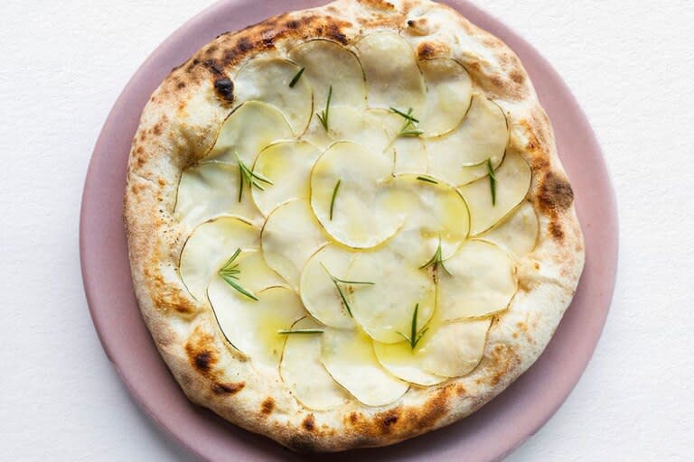 La pizza blanca de Mudrá, con crema de ajo ahumado, láminas de papa, romero fresco y aceite de oliva.