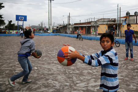 Children play at a basketball court covered with ash after Guatemala's Fuego volcano erupted violently, in Guatemala City, Guatemala June 3, 2018. REUTERS/ Luis Echeverria