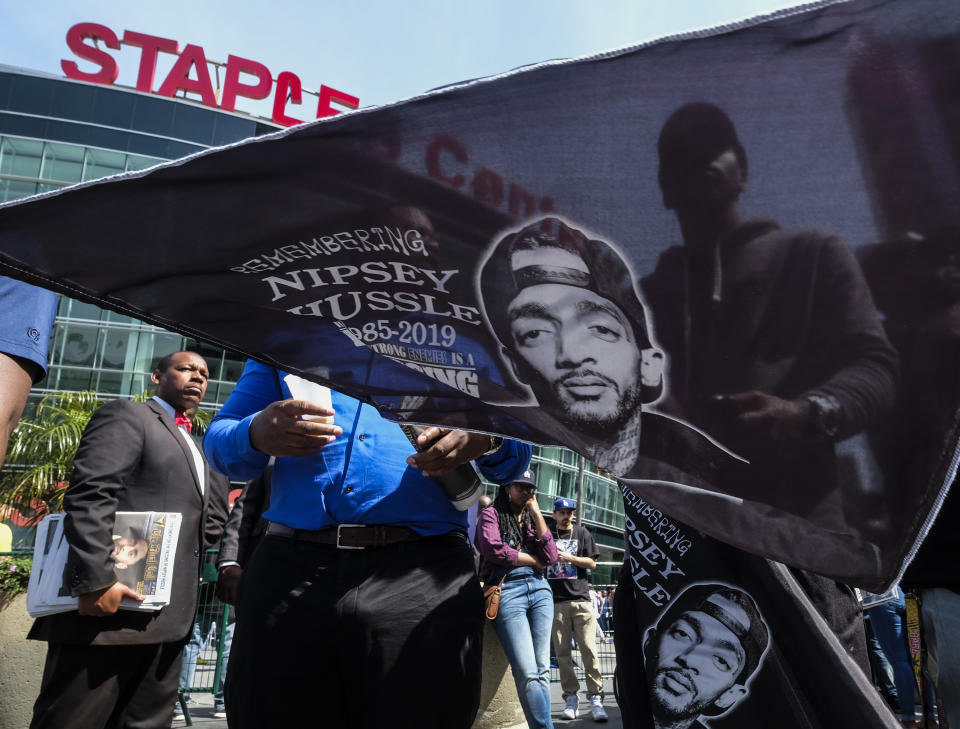 A fan of rapper Nipsey Hussle holds a flag with Hussle's image on it as he attends a public memorial at Staples Center in Los Angeles, Thursday, April 11, 2019. Hussle was killed in a shooting outside his Marathon Clothing store in south Los Angeles on March 31. (AP Photo/Ringo H.W. Chiu)