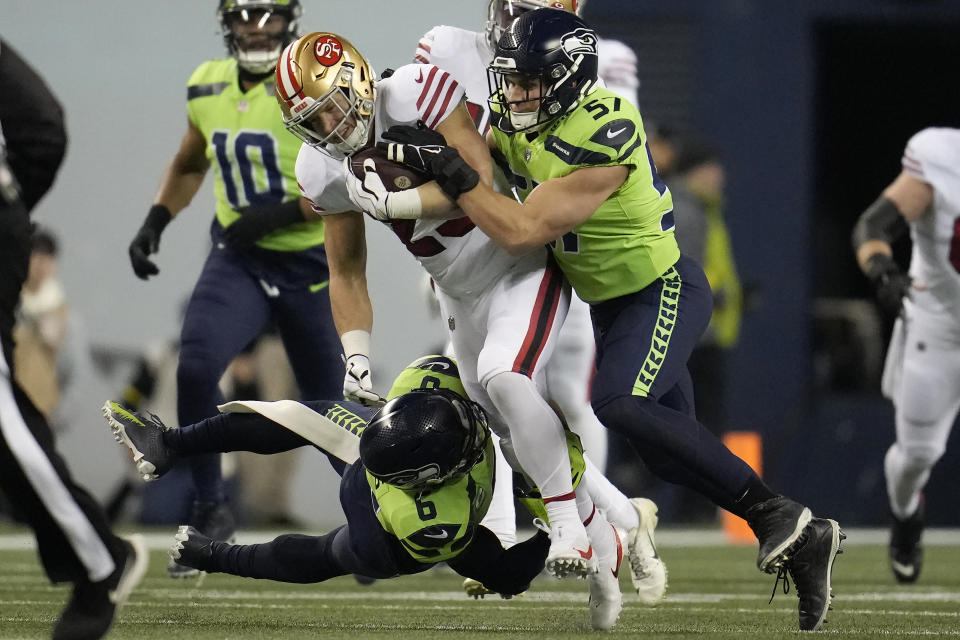 San Francisco 49ers running back Christian McCaffrey, middle, runs against Seattle Seahawks safety Quandre Diggs, bottom, and linebacker Cody Barton (57) during the first half of an NFL football game in Seattle, Thursday, Dec. 15, 2022. (AP Photo/Marcio Jose Sanchez)