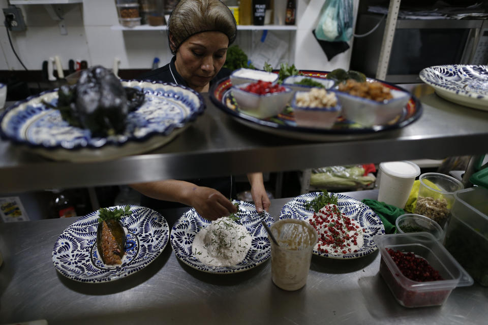 In this Sept. 13, 2019 photo, a cook assembles chiles en nogada for clients at Testal restaurant in central Mexico City. Testal has dedicated nearly an entire kitchen to the production of the emblematic dish, selling around 150 chiles per day, and attempting to more than double the 3000 chiles they sold last year during the short season. (AP Photo/Rebecca Blackwell)