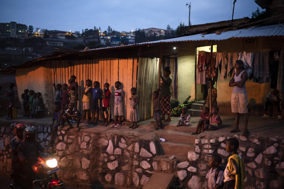 In this Sept. 9, 2019 photo, people stand outside a house at dusk in Kigali, Rwanda. An estimated 60 million people in the world will die this year, and half will lack death certificates _ and so have no recorded cause of death. Most will be in low- and middle-income countries, particularly in Africa and parts of Asia. (AP Photo/Felipe Dana)