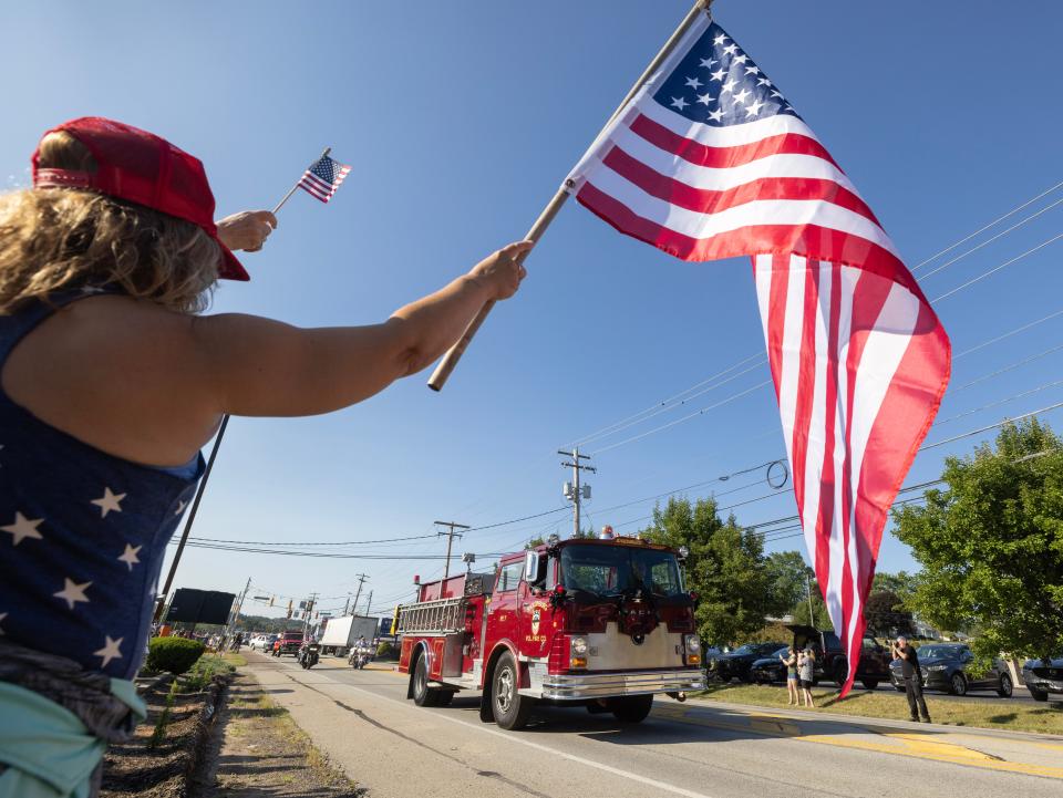 Merri Carbo,waves a flag outside Freeport Senior High in Freeport Pennsylvania as a motorcade of fire engines and EMS vehicles headed off to the funeral of Corey Comperatore the Buffalo Township man killed at SaturdayÕs rally for former President Donald Trump from a would-be assassinÕs stray bullet. Kevin Whitlock / Massillon Independent