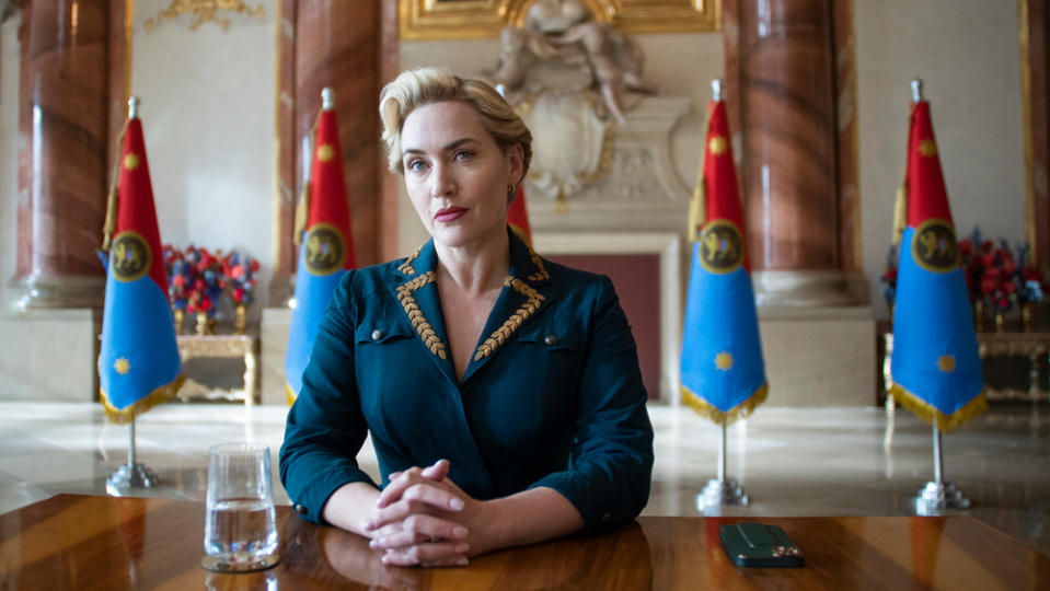 Kate Winslet as Elena Vernham seated at a desk with a row of flags behind her in 'The Regime.'
