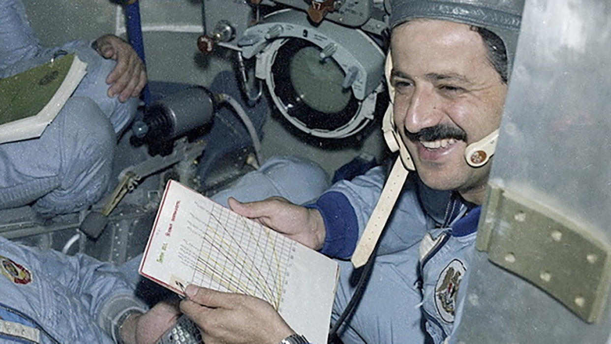  A smiling man with a mustache holds a clipboard. 