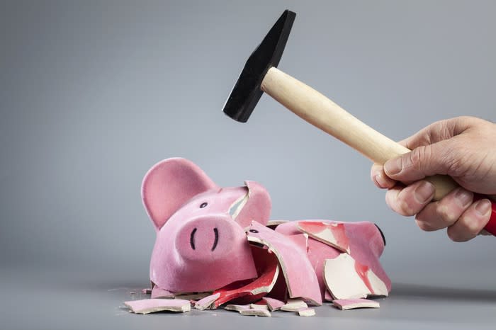 A man's hand holds a hammer over a broken piggy bank