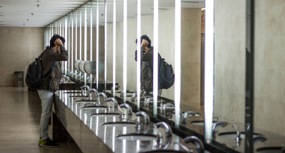 A man looks in the mirror, touching his hair in a public bathroom. Hobart is considering adding gender neutral signs to their public bathrooms.