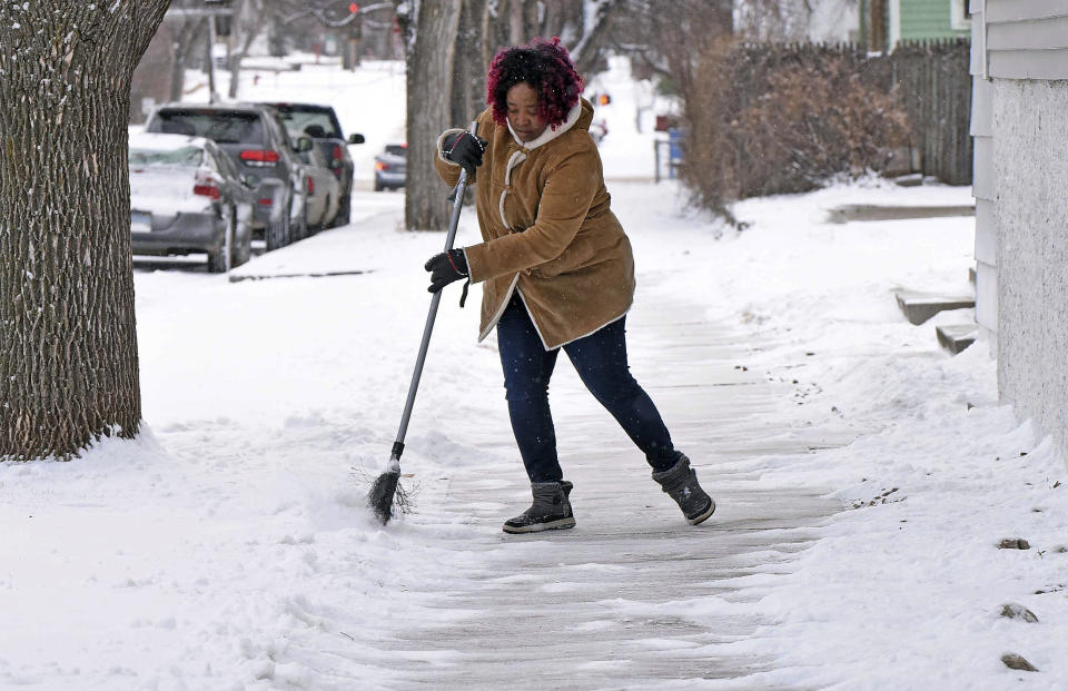 Josephine Wiea sweeps the sidewalk of snow at the International Church Thursday, March 21, 2024 in Bismarck, N.D. Parts of Montana, the Dakotas, Minnesota, Illinois and Wisconsin are under winter weather advisories, with snow expected to start falling Thursday in some areas. Minnesota could see a foot of snow over the weekend, and parts of New England could also see 12 to 18 inches (30 to 45 centimeters) in the coming days. (Tom Stromme/The Bismarck Tribune via AP)
