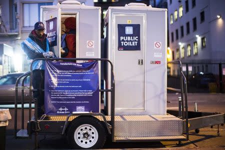 A visitor enters a portable toilet facility held open by an attendant in the Tenderloin District in San Francisco, California December 30, 2014. REUTERS/Stephen Lam